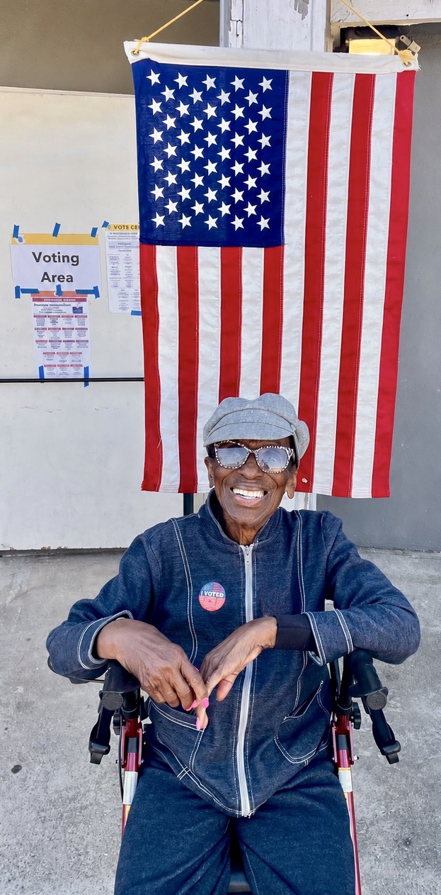 Ethel L. Lee, 100 years old, with her I VOTED sticker under the flag at an LA County vote center.